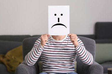 Genç adam evde koltukta otururken sayfaya çizilmiş ifade arkasında yüz gizleme