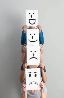 Genç kadın yüzleri yaprak kağıt üzerinde açık renkli çizilmiş emoticons ile arkasında saklanıyor