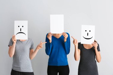 Genç kadın yüzleri yaprak kağıt üzerinde açık renkli çizilmiş emoticons ile arkasında saklanıyor