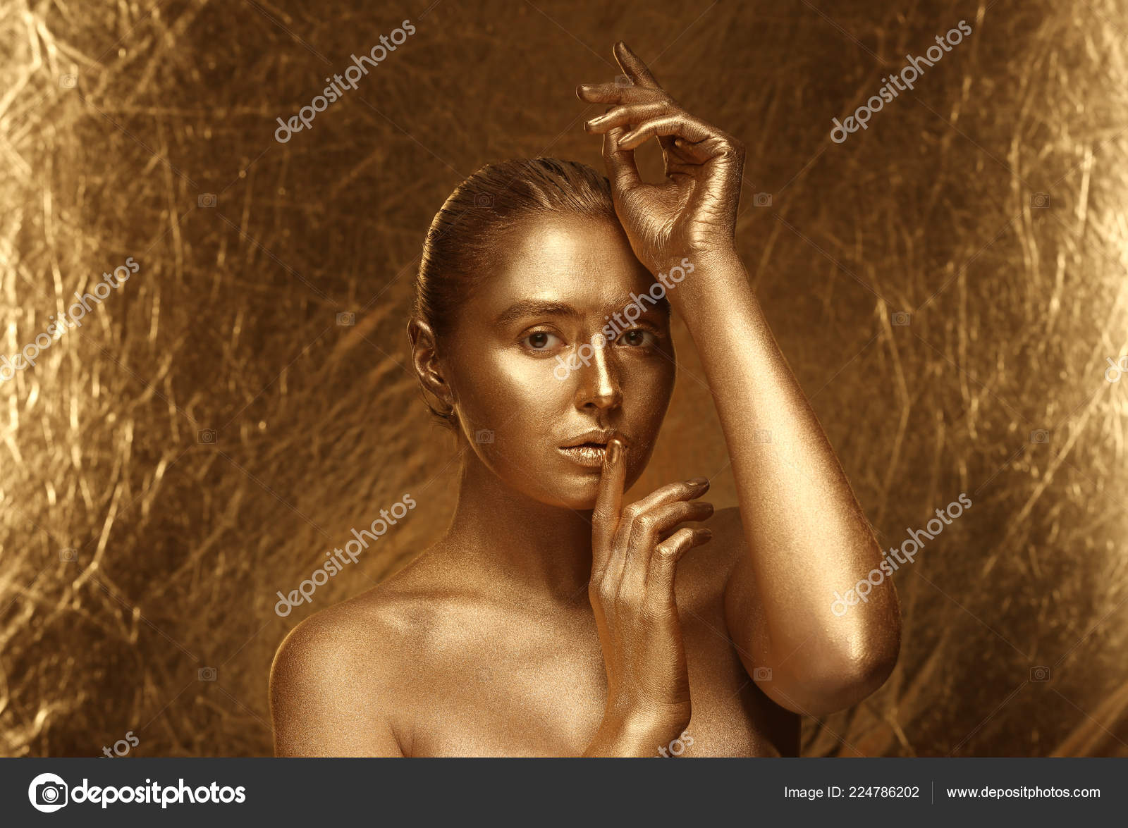 Artist painting beautiful young model in gold color paint, body