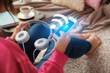 Kadın evde ücretsiz Wi-Fi kullanarak akıllı telefon ve kulaklık ile