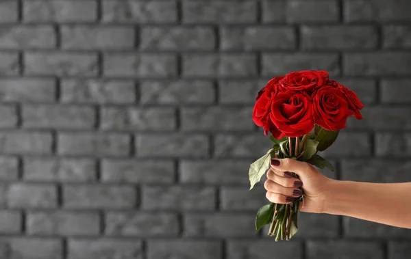 Female hand with bouquet of beautiful roses against dark brick wall