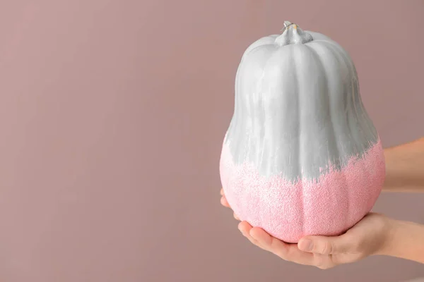 Woman holding painted pumpkin on color background