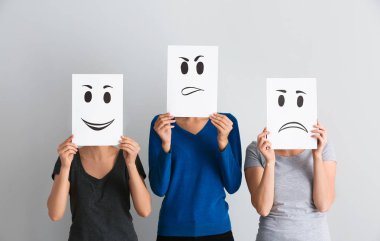 Genç kadın yüzleri yaprak kağıt üzerinde açık renkli çizilmiş emoticons ile arkasında saklanıyor