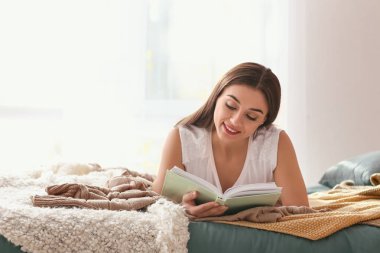 Kadın yatak odasında kitap okuyor.