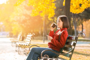 Sonbahar Park ahşap bankta oturmuş kahve olan güzel kadın