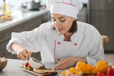 Genç kadın şef mutfakta lezzetli yemek üzerine sos dökme