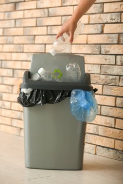 Tuğla duvar yakınındaki çöp kutusu içine plastik şişe atma kadın