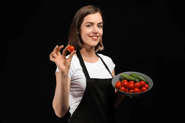 Young female chef with vegetables on dark background