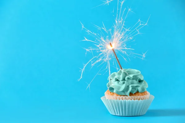 Tasty cupcake with sparkler on color background