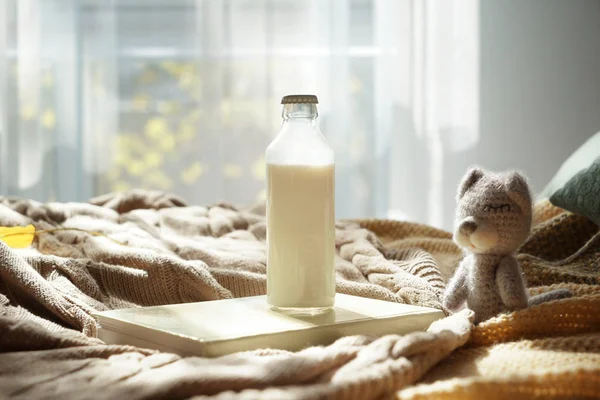 Baby toy and bottle of milk on warm plaid indoors