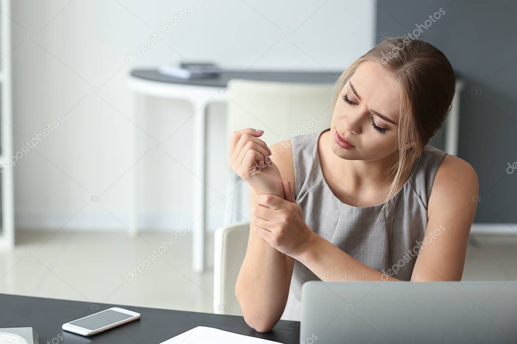 Young woman suffering from pain in wrist at workplace