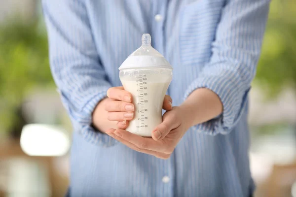 Woman holding feeding bottle of milk for baby, closeup