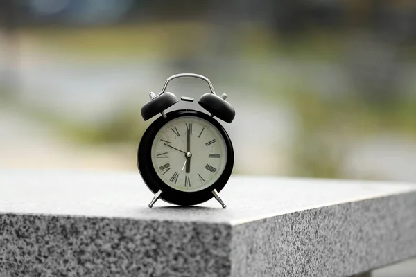 Alarm clock with Rome numbers on blurred background outdoors