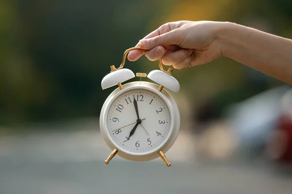 目覚まし時計を持っている女性の手がぼやけて背景屋外 — ストック写真