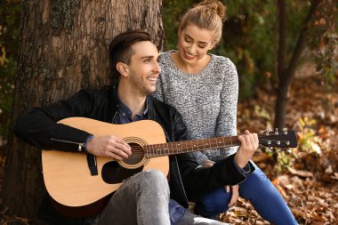 Yakışıklı genç adam gitar ve sonbahar Park'ta dinlenme sevgili