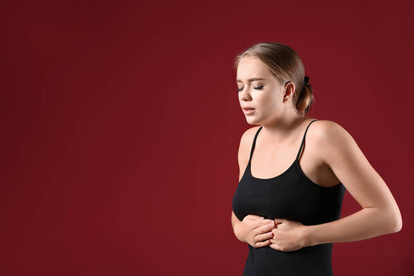Young woman suffering from abdominal pain on color background