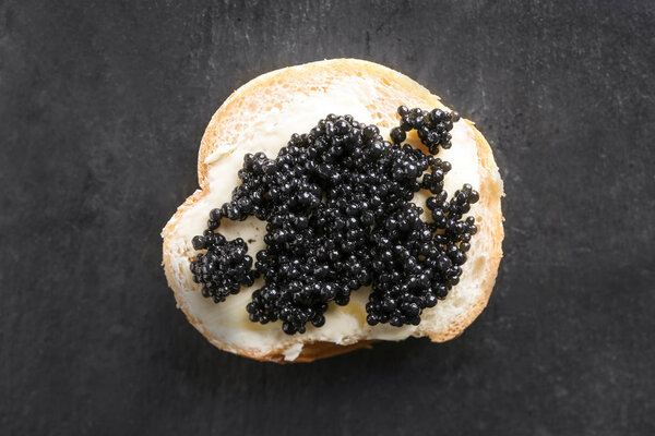 Delicious sandwich with black caviar on dark table