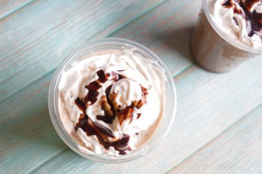 Soğuk kahve krem şanti ve ahşap masa üzerinde ıslak plastik bardak çikolata kaplı