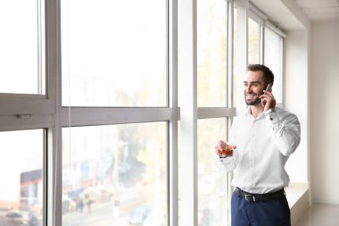 Cam pencere yakınındaki telefonla konuşurken viski ile genç adam