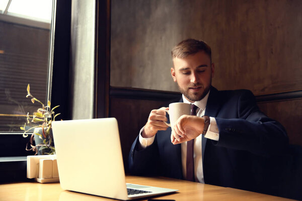 Businessman looking at watch while sitting in cafe