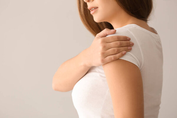 Young woman suffering from pain in shoulder on light background