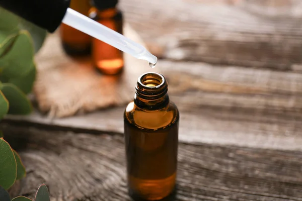 Eucalyptus essential oil dripping from pipette into bottle on wooden table