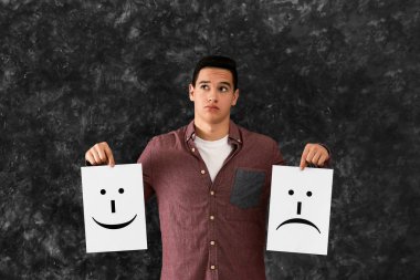 Kağıda çizilmiş emoticons ile gri arka plan üzerinde tutan genç adam