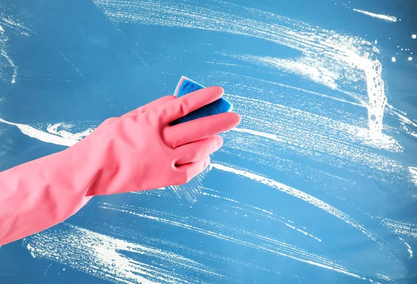 Woman cleaning glass with sponge on color background