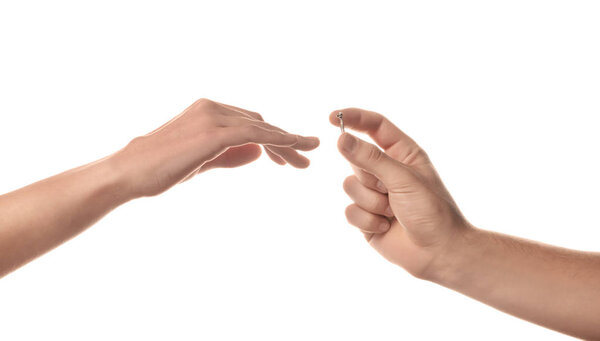Man putting engagement ring on fiancee's finger on white background