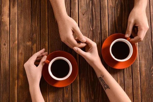 Young couple with cups of coffee holding hands on wooden table