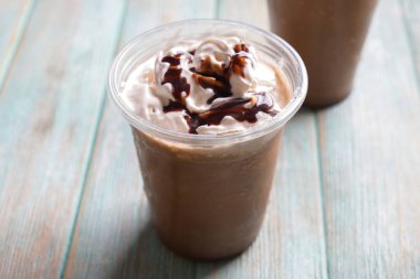 Soğuk kahve krem şanti ve ahşap masa üzerinde ıslak plastik bardak çikolata kaplı