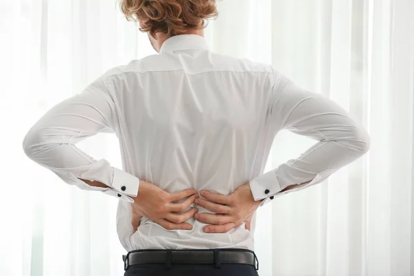 Young businessman suffering from back pain near window