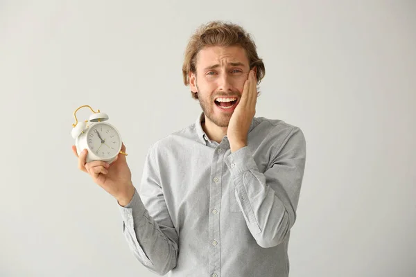 Stressed man with alarm clock on light background