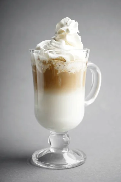 Cold coffee covered with whipped cream in glass on grey background