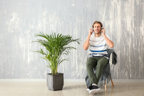 Young man listening to music while sitting in armchair near grey wall