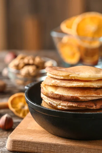 Pan with stack of hot pumpkin pancakes on wooden board