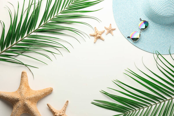 Composition with beach hat, sunglasses, tropical leaves and starfishes on white background