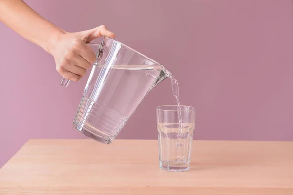 Woman pouring fresh water from jug into glass on wooden table