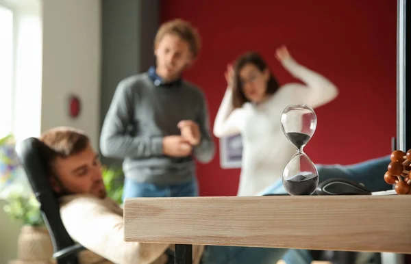Hourglass on table of sleeping lazy worker in office