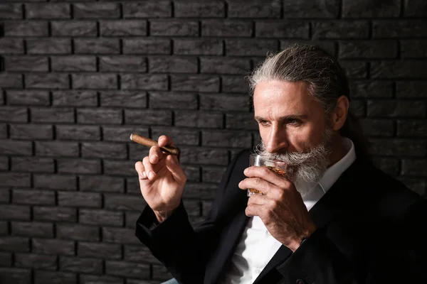 Старший Мужчина Пьет Виски Курит Сигару Возле Темной Кирпичной Стены — стоковое фото