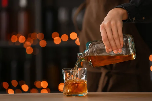 女酒保将威士忌从瓶子倒进桌子上的玻璃里 — 图库照片