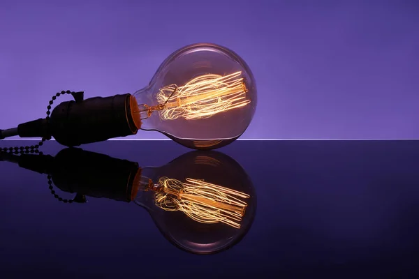 Glowing retro light bulb with reflection on color table