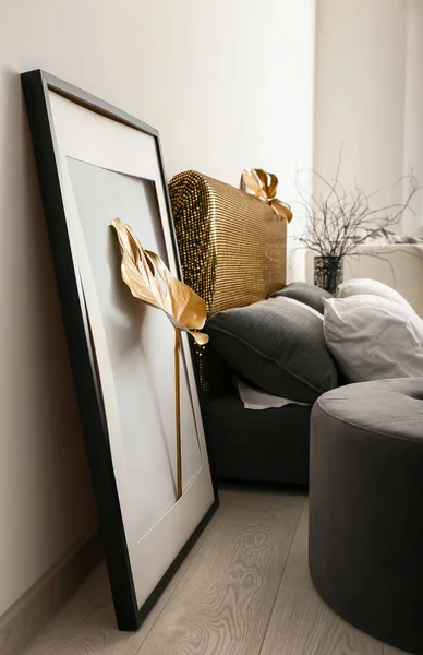 Big frame with golden tropical leaf near bed in room