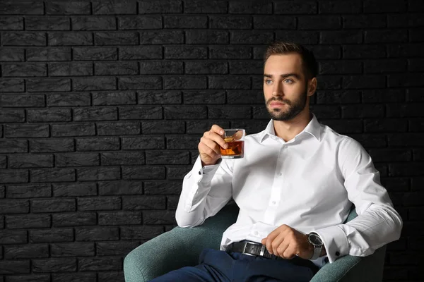 青年実業家暗いレンガの壁の近くのウィスキーを飲みながら — ストック写真