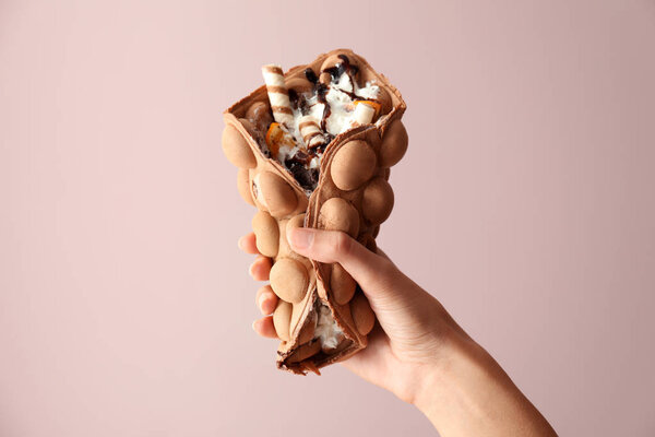 Женская рука с вкусной сладкой вафлей пузыря на цветном фоне
