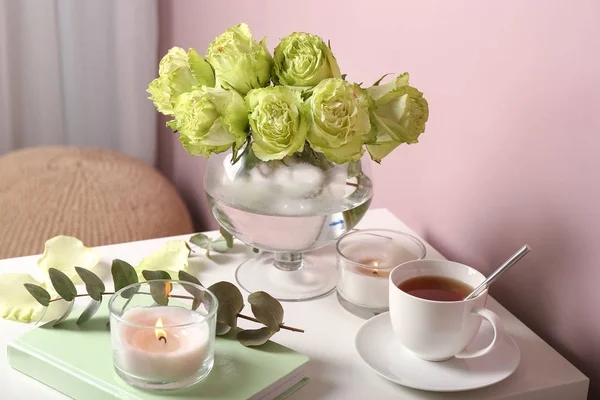 Bouquet of beautiful green roses, candle and cup of tea on table