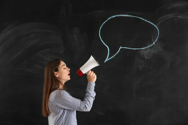 Young woman with megaphone near blank speech bubble drawn on blackboard