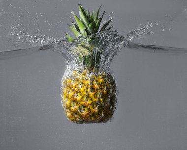 Ananas düşen suya gri arka plan üzerinde