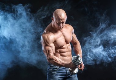 Duman koyu arka plan üzerinde halter ile kas vücut geliştirmeci